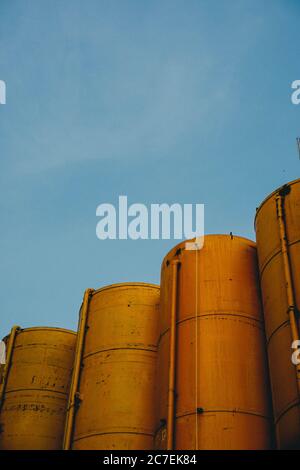 Vertikale Aufnahme von vier gelben Metallsilos mit dem blauen Himmel im Hintergrund Stockfoto