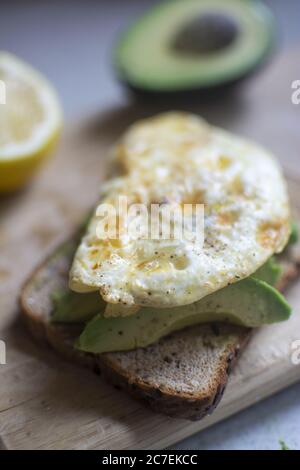 Vertikale selektive Nahaufnahme von Spiegelei auf Ein Avocado Toast auf einem Schneidebrett Stockfoto