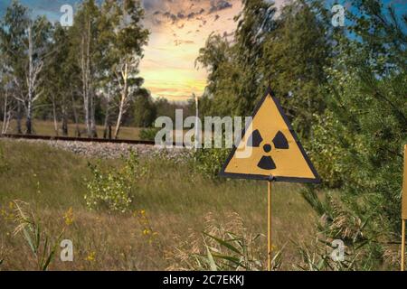 Gelbes Warnschild für Strahlung in der tschernobyl-Sperrzone, gefährlicher Rotwald im Hintergrund. Am späten Nachmittag wunderschöne goldene Sonnen Stockfoto