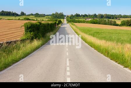 Gerade Landstraße zwischen sanften Hügeln im Frühling Stockfoto