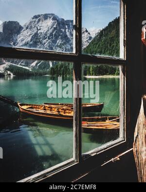 Vertikaler Schuss aus dem alten Fenster von Holzbooten auf Friedlicher See Prags Italien umgeben von Bergen Stockfoto