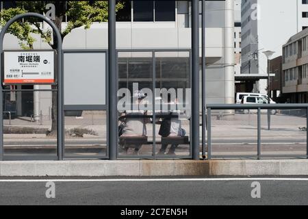 MATSUYAMA, JAPAN - 23. Sep 2019: Eine horizontale Aufnahme von zwei Freunden, die sich gegenseitig von ihren Tagen erzählen, während sie auf den Bus warten Stockfoto