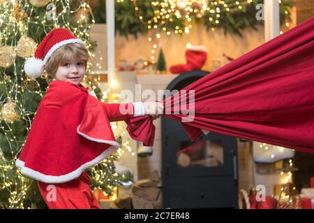 Kleiner Weihnachtsmann zieht riesige Tasche von Geschenken auf Weihnachten Hintergrund. Weihnachtsmann Kind. Frohe weihnachten und ein glückliches neues Jahr. Lieferung weihnachtsgeschenke. Stockfoto