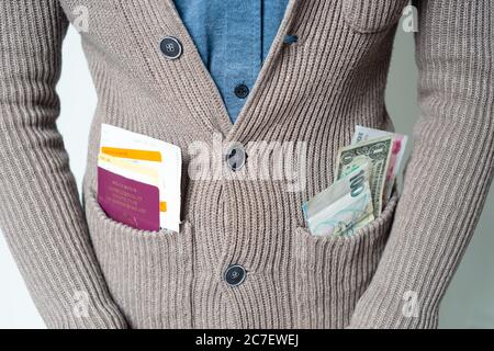 Junger Mann in Strickjacke mit Pass und Tickets und verschiedenen Währungen in der Tasche, Konzept - Reisen, Reisende, weltweit Stockfoto