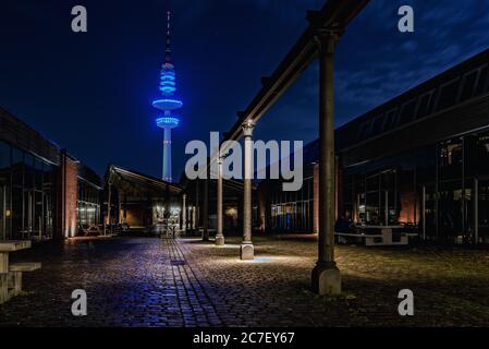 Horizontale Aufnahme eines Funkturms mit Leuchten auf dem Straße mit Cafés in der Nacht unter dem bewölkten Himmel Stockfoto
