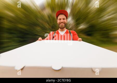 Mann mit Lebensmittelzustellung in roter Uniform mit einer großen Schachtel Pizza aus nächster Nähe. Schnelle Pizzalieferung. Stockfoto