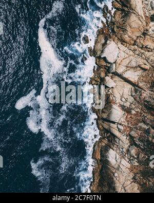 Vertikale Aufnahme von felsiger Küste neben einem Körper Von Wasser mit Wellen, die die Felsen bespritzen Stockfoto