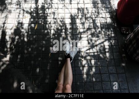 High-Angle-Aufnahme einer Person, die graue Sneakers trägt Ein grauer Fliesenboden Stockfoto