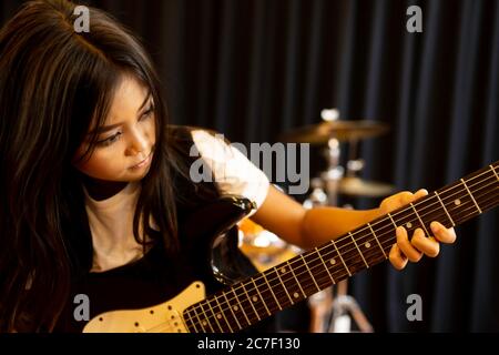 Ein süßes asiatisches Grundschulmädchen, das lange Haare hat und ernsthaft eine E-Gitarre für einen Rocksong spielt. Stockfoto