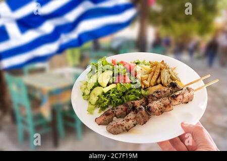 Hand hält eine traditionelle griechische Schweinefleisch Souvlaki Teller mit gebratenen Kartoffeln und grünem Salat. Stockfoto