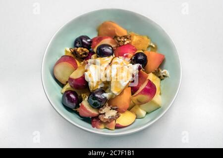 Draufsicht auf einen hausgemachten griechischen Obstsalat mit Nüssen, Apfel, Pfirsich, Trauben und Joghurt mit Honig. Stockfoto