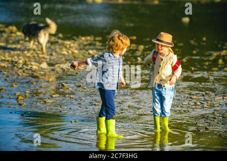 Kinder spielen am Stony River. Sommeraktivitäten für Kinder. Kleiner Junge und Mädchen wirft Steine ins Wasser am Ufer eines Sees oder Flusses. Stockfoto