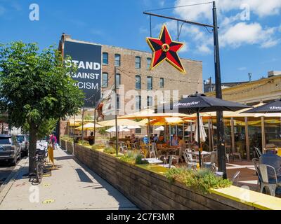 Big Star Restaurant im Freien, sozialer Abgrenzung auf dem Bürgersteig. Stellen Sie sich gegen Rassismus Banner auf Gebäude im Hintergrund. Damen Avenue, Wicker Park Nachbarschaft, Chicago, Illinois. Stockfoto