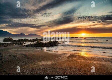 Der lebendige goldene Sand am Strand von Kaikoura bei einem dramatischen, farbenfrohen Sonnenaufgang, wenn die Sonne über dem Horizont über dem Meer aufgeht Stockfoto