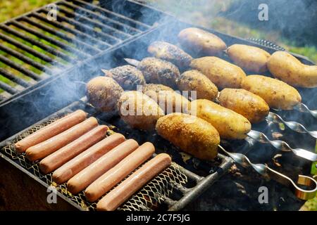 Gegrillte Würstchen und Kartoffeln auf Spieß Grill im Freien. Stockfoto