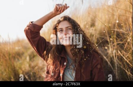 Lockiges Modell in einer braunen Jacke lächelnd und werfendes Glitzer In der Luft Stockfoto