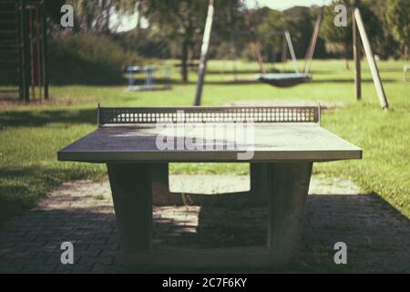 Stein-Tennis-Tisch im Park mit einem Spielplatz in Der Hintergrund an einem sonnigen Tag Stockfoto