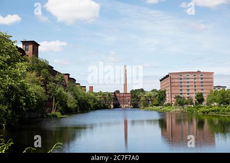 Ehemalige Textilfabriken säumen den Nashua River in Nashua, New Hampshire, USA, heute Clocktower Place und Apartments in Cotton Mill mit Millyard Smokestack. Stockfoto