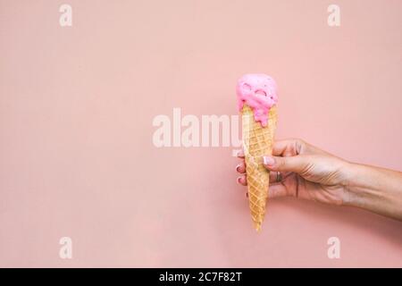 Mädchen Hand hält geschmolzene rosa Erdbeere Eis-Konus auf rosa Hintergrund. Stockfoto