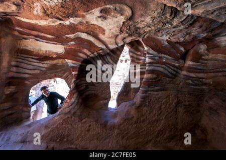 Ein Mann, der in eine der spektakulären Sandsteinhöhlen von Petra in Jordanien blickt. Petra wurde möglicherweise bereits 312 v. Chr. gegründet. Stockfoto