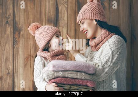 Winterporträt einer glücklichen, liebevollen Familie in Strickmützen, Snoods und Pullovern. Mutter und Kind Mädchen Spaß haben, spielen und lachen auf braunem Holz Stockfoto