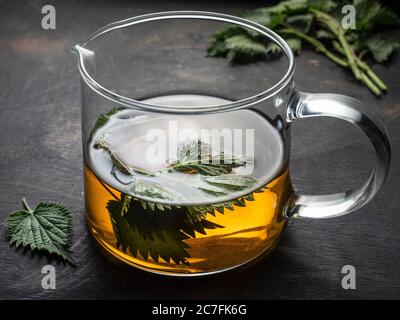 Frischer Brennnesseltee in Glaskanne auf Holztisch. Stockfoto