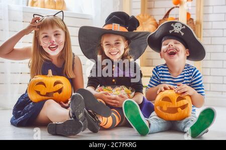 Fröhlicher Bruder und zwei Schwestern an Halloween. Lustige Kinder in Karnevalskostümen drinnen. Fröhliche Kinder spielen mit Kürbissen und Süßigkeiten. Stockfoto