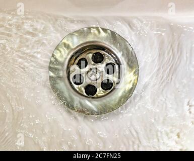 Ablassen von Wasser mit einem Edelstahlgitter in einem alten, lang genutzten Waschbecken im Badezimmer Stockfoto