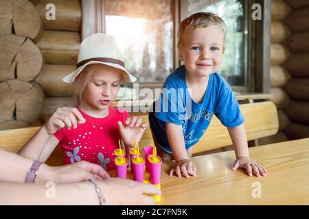 Zwei niedliche liebenswert kaukasischen blonde kleine Geschwister sitzen am Tisch Haushof und haben Spaß Verkostung Mutter hausgemachte Obst Eis. Junge glückliche Schwester und Stockfoto