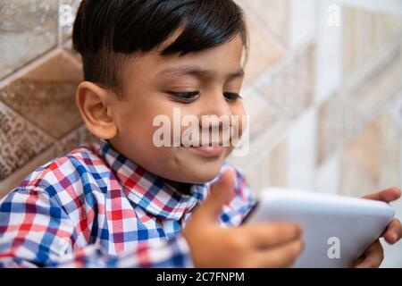 Indoor-Bild von kleinen Jungen mit Smartphone und spielen Videospiel in der Freizeit. Stockfoto