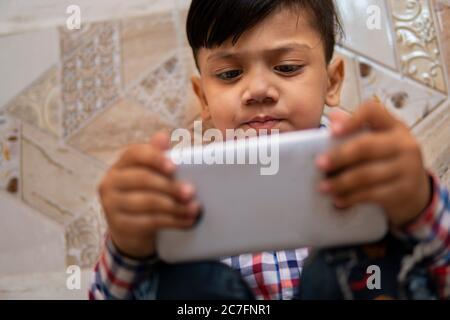 Indoor-Bild von kleinen Jungen mit Smartphone und spielen Videospiel in der Freizeit. Stockfoto