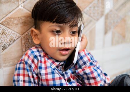 Indoor-Bild von niedlichen kleinen Jungen im Gespräch auf dem Smartphone. Stockfoto