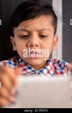 Indoor-Bild von kleinen Jungen mit Smartphone und spielen Videospiel in der Freizeit. Stockfoto