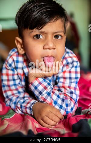 Portrait von niedlichen wütend kleinen Jungen auf dem Bett liegen und seine Zunge aus, während Blick auf die Kamera. Stockfoto