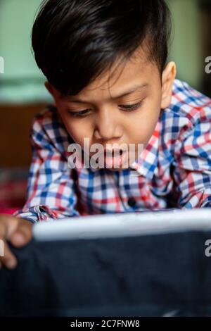 Innenbild des kleinen Jungen auf dem Bett mit den Händen auf dem Kinn liegen und Video auf dem Smartphone in zu Hause. Stockfoto