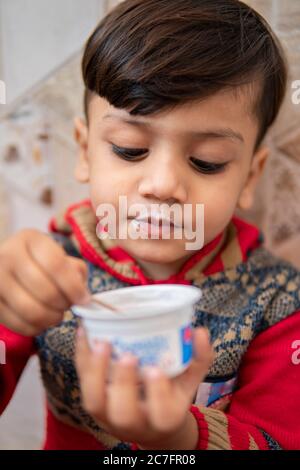 Nahaufnahme von niedlichen kleinen Jungen in roten Kleid, Essen Tasse Eis mit Löffel zu Hause. Stockfoto