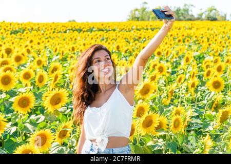 Ein schöner Influencer begrüßt den Sommer, indem er ein Selfie in einem wunderschönen Feld von gelben Sonnenblumen macht Stockfoto