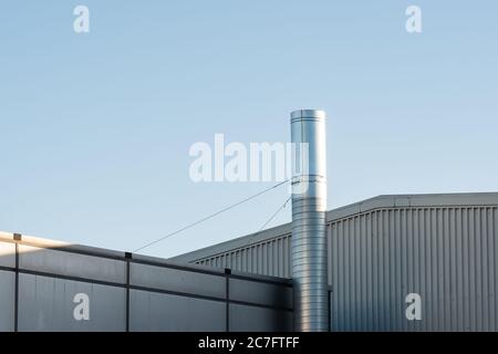 Außenansicht einer modernen, Stahl strukturierten Fabrik an einem klaren, winterlichen Tag. Ein großer Industriekamin ist sichtbar, der von Drahtankern gehalten wird. Stockfoto