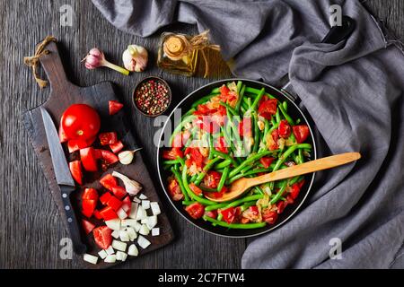 Karibische Stir-frittierte grüne Bohnen mit Zwiebeln und Tomaten, Fry bodi in einer Pfanne auf einem Holztisch mit Zutaten, flach legen, horizontale Ansicht Stockfoto