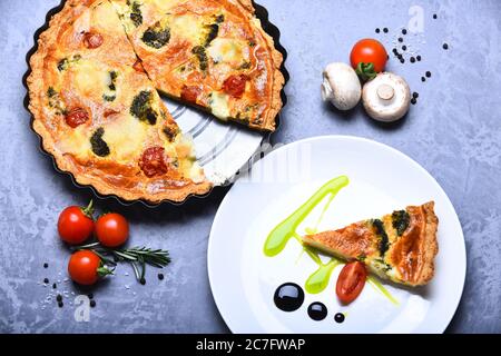 Vegetarische Pizza mit Tomaten, Brokkoli und Käse auf grauem Hintergrund. Pizza Pie in Metall Backform Stück auf dem Teller serviert. Traditionelles rustikales Küchenkonzept. Vegane Küche im Café oder Restaurant. Stockfoto
