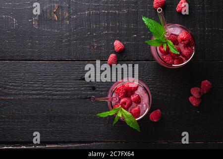 Frisch eiskalter Beerensaft-Drink mit Minze, Sommerlimonade in zwei Gläsern mit Strohhalmen auf dunklem Holzhintergrund, Draufsicht Kopierraum Stockfoto