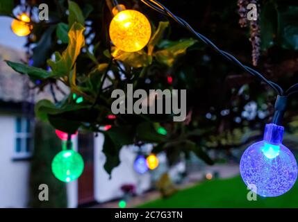 Solar-Party LED-Lichter auf einem Baum, wie in einem großen Garten während einer Sommerparty am frühen Abend gesehen beleuchtet. Stockfoto