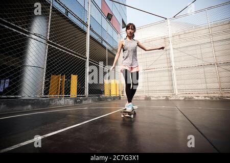 Schöne junge asiatische weibliche Skateboarder üben Skateboarding im Freien
