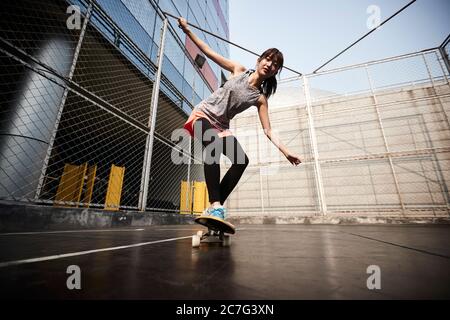 Schöne junge asiatische weibliche Skateboarder üben Skateboarding im Freien Stockfoto