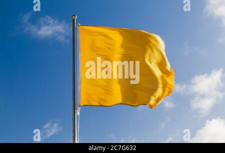 Gelbe Warnflagge auf einer Strandwache, die bei starkem Wind über blauem Himmel winkt Stockfoto