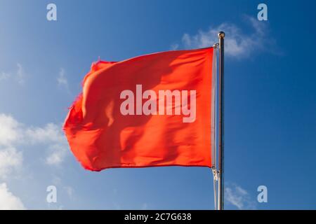 Schwimmen ist verboten. Rote Warnflagge auf einer Strandwache, die bei starkem Wind über blauem Himmel winkt Stockfoto