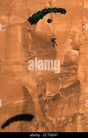 USA, Utah, Moab, EIN Base Jumper steigt in seinem Fallschirm von der 400 Fuß hohen vertikalen Seite des Tombstone im Kane Springs Canyon ab. Beachten Sie seinen Schatten auf der Klippe. Stockfoto