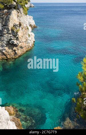 Die Sommersonne lädt das klare, klare, blaue und türkisfarbene Wasser zum Leuchten in einer Bucht der Insel Skopelos ein und Sie wollen sich zur Erfrischung einlassen. Stockfoto