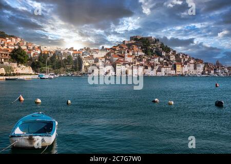 Altstadt von Sibenik, Kroatien von einem entfernten Strand aus gesehen. Kleines altes blaues Schiff verankert. Blick auf die mediterrane typische traditionelle Meereslandschaft Stockfoto