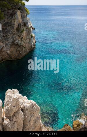 Die Sommersonne lädt das klare, klare, blaue und türkisfarbene Wasser zum Leuchten in einer Bucht der Insel Skopelos ein und Sie wollen sich zur Erfrischung einlassen. Stockfoto